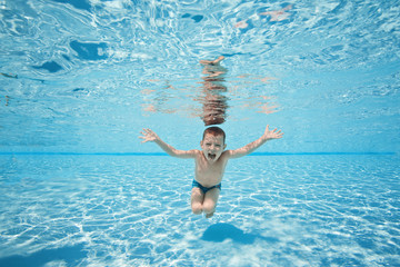 Happy young boy swim and dive underwater, kid breast stroke with fun in pool. Active healthy lifestyle, water sport activity and lessons with parents on summer family vacation with child