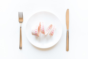 Wall Mural - Measuring tape in a plate with cutlery on a white background. diet concept
