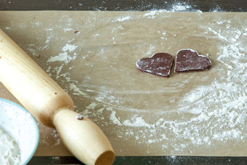 two pieces of homemade chocolate chip cookies in the form of a heart on a table in white flour.