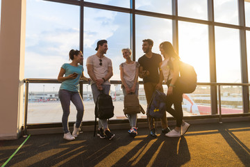 Wall Mural - young people group in airport lounge near windows waiting departure speaking happy smile mix race fr