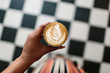 © Kristen Curette Photography LLC/Stocksy - A woman holding a cortado and looking down at a checkered floor.