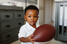 A Young Toddler Holding A Football Indoors