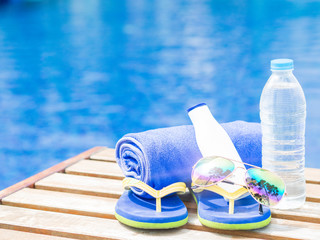 Wall Mural - flip flops, sunglasses, blue towel and sunscreen at the side of swimming pool. Vacation, beach, summer travel concept