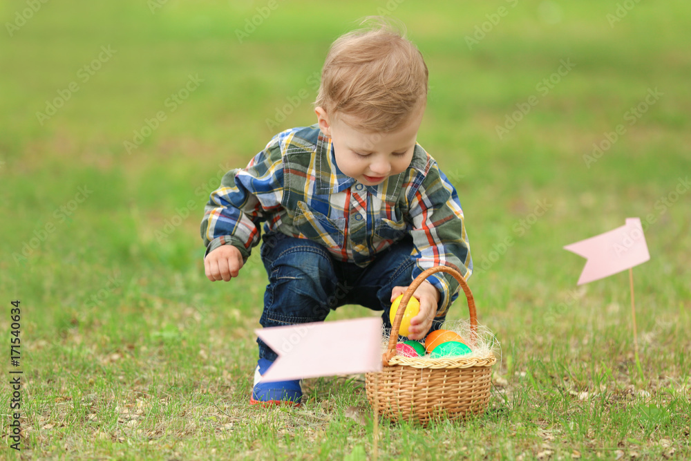 Cute little boy with basket on green grass. Easter egg hunt concept