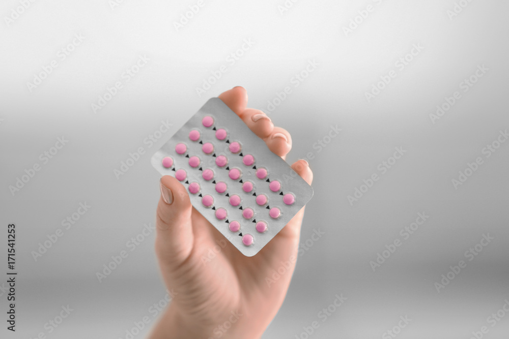 Female hand with hormonal pills on blurred background