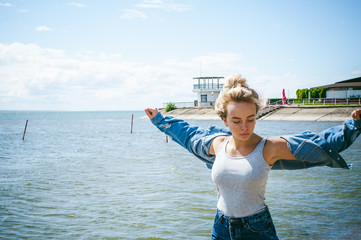 young beautiful woman in jeans clothes outdoors. portrait of a girl with freckles on her face, stylish girl on sea beach, on a sunny summer autumn day. stretched out her arms