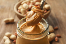 Spoon And Glass Jar With Creamy Peanut Butter On Kitchen Table, Closeup