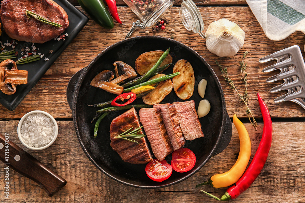 Composition with delicious steak in frying pan on table