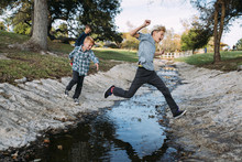 Brothers Jumping Over Stream In Park