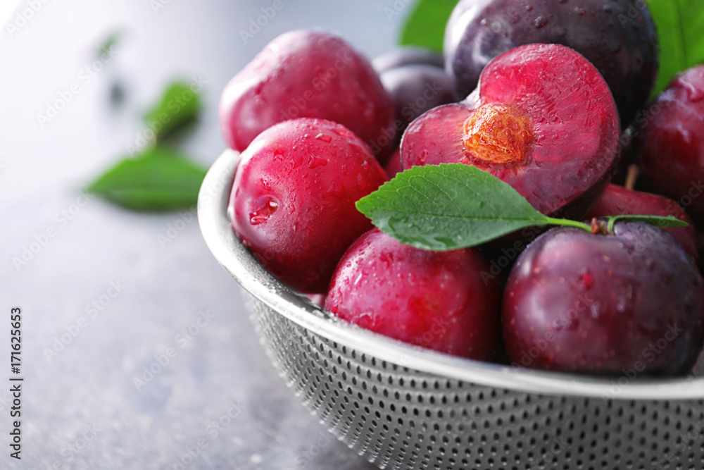 Sieve with fresh ripe plums on table, closeup