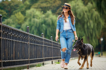 A young girl is walking with a German shepherd dog in the park.