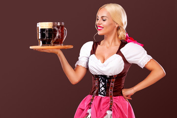 Wall Mural - Closeup portrait of Oktoberfest girl - waitress, wearing a traditional Bavarian dress, serving big beer mugs on brown background.