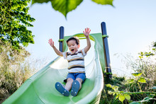 Asian Kid Playing On A Slide In The Playground