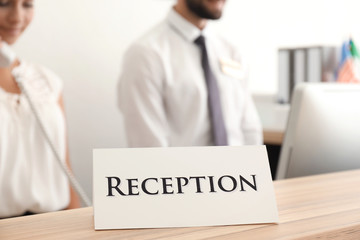 Reception sign and two busy hotel workers on background