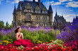 A beautiful woman, a princess in a red dress, sits by in a blooming garden. An ancient castle in the background. Medieval fantasy, European palace