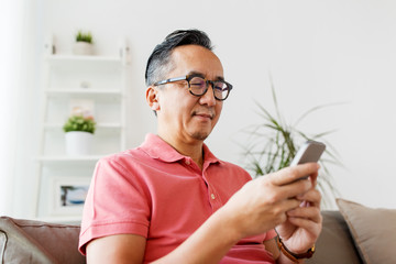 asian man with smartphone sitting on sofa at home