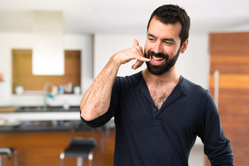 Handsome man with beard making phone gesture inside house