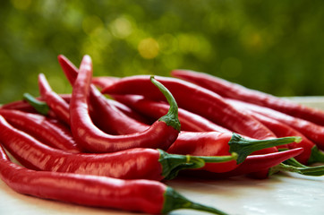 Many hot red chili peppers on white wooden table on blurred green nature background. Close up view