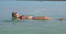 Pregnant Woman Bathing In Dead Sea. Son Taking Her Hand And Pulling As She Floating In Salt Water. Family Spending Holidays On Resort In Israel