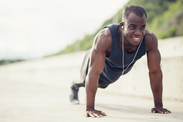 Young athletic man doing push-ups. Fitness model doing outdoor workout. Muscular and strong guy exercising.