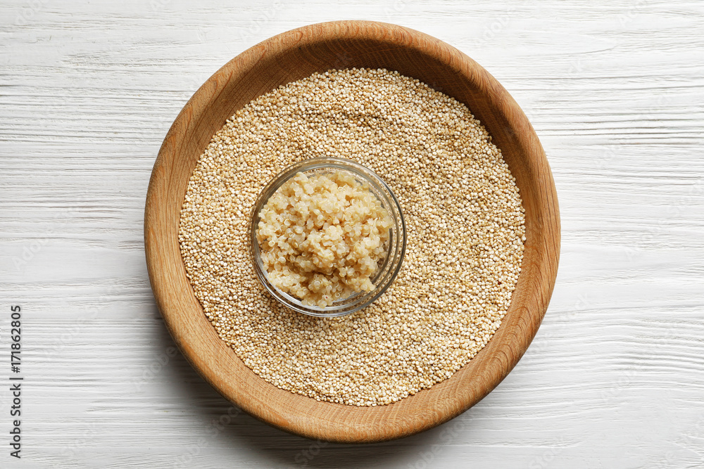 Bowls with boiled and raw quinoa grains on wooden table