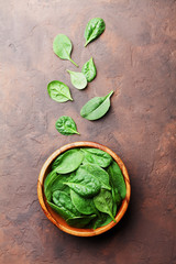 Wall Mural - Heap of baby spinach leaves in wooden bowl on rustic table top view. Organic diet food.