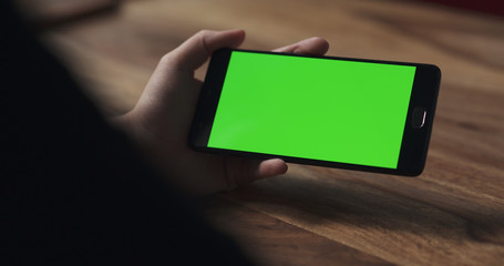 Wall Mural - female teen girl hold smartphone with green screen over wood table