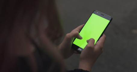 female teen girl using smartphone with green screen sitting outdoors