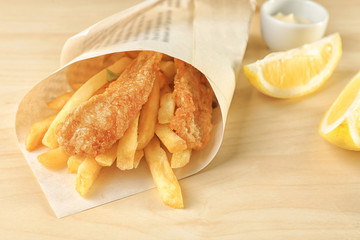 Wall Mural - Tasty fried fish and potato chips rolled in paper on wooden table