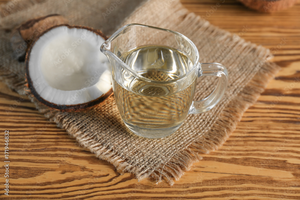 Ripe coconut and pitcher with oil on wooden background