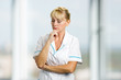 © DenisProduction.com - Confident thinking mature nurse. Portrait of thoughtful mature medical doctor holding chin on hand and thinking on blurred background.
