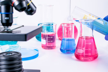 Sticker - hand of scientist pouring into flask colorful liquid. examining samples in laboratory and close up of microscope . laboratory science, clinic and research concept. 