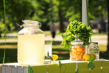 Lemonade in glass jar with tap on wooden stand outdoors