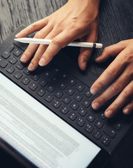 Closeup view of two male hands typing on electronic tablet keyboard-dock station. Man working at office and using electronic pen.Vertical.Cropped.