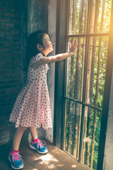 Wall Mural - Asian girl with beautiful dress looking at the sunrise standing near the window.