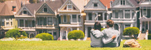 San Francisco Tourist Attraction At Alamo Square, The Painted Ladies Banner Panorama, California Travel. Couple Tourists Relaxing In Grass Enjoying Popular Destination. People Lifestyle