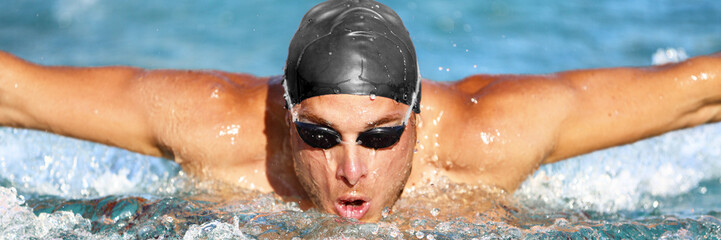 Wall Mural - Swimmer. Man swimming butterfly strokes in pool competition. Competitive male sport athlete swimmer wearing swimming goggles and cap. Young caucasian fitness model face portrait.