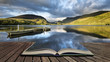 Stunning dramatic stormy sky formations over breathtaking mountain lake landscape with rowing boats in foreground concept coming out of pages in book