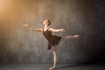 Wall Mural - beautiful young blonde ballet dancer in a black dress, white pantyhose and bouillant pointes dancing Russian ballet in a dark dance studio