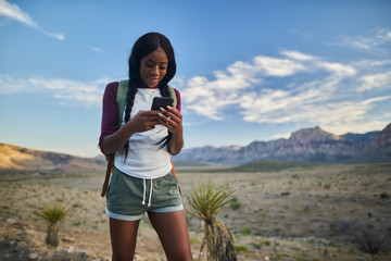 Wall Mural - athletic african american woman with backpack looking at smart phone while hiking in red rock canyon