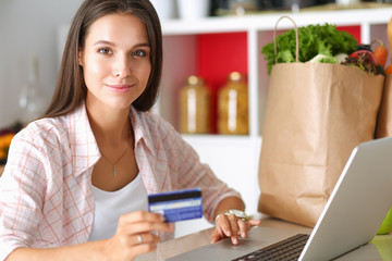 Smiling woman online shopping using tablet and credit card in kitchen