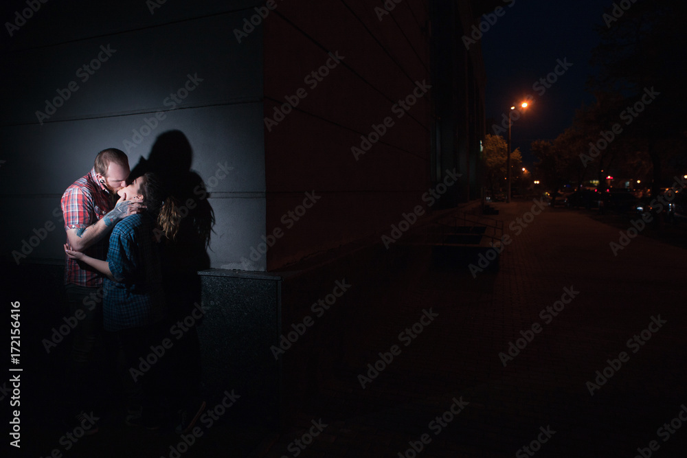Passionate couple kissing in shadows against a dark wall, forbidden romance tension