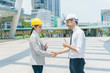 © bixpicture - Two engineer handshaking after success project at site. Couple wearing safety helmet and handshake with city background. Concept of business partnership meeting.