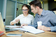 © pressmaster - Young financial managers analyzing statistics while having working meeting at spacious open plan office, handsome man holding paper cup of coffee in hand