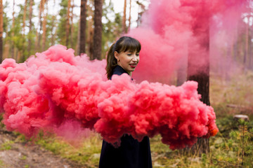 Young woman in forest having fun with red smoke grenade, bomb