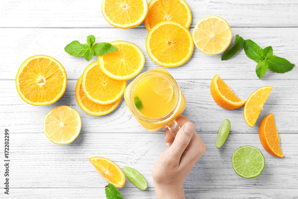 Woman holding mason jar with fresh orange juice on table