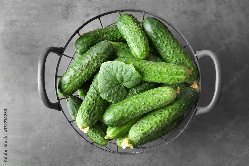 Many green fresh cucumbers in metal basket on gray table