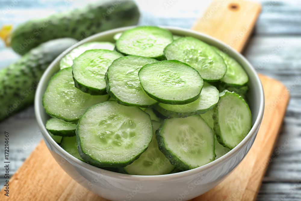 Bowl with fresh sliced cucumbers on wooden board