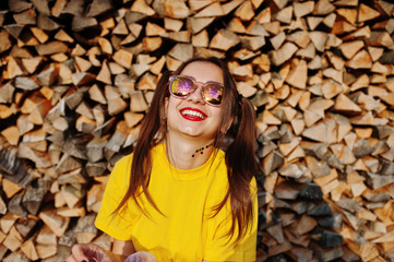 young funny girl with bright make-up, tail hair wear on yellow shirt and sunglasses against wooden b