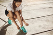 © Liubov Levytska - Woman runner tying up her laces getting ready for a long run into successful fitness career. Urban sport concept.